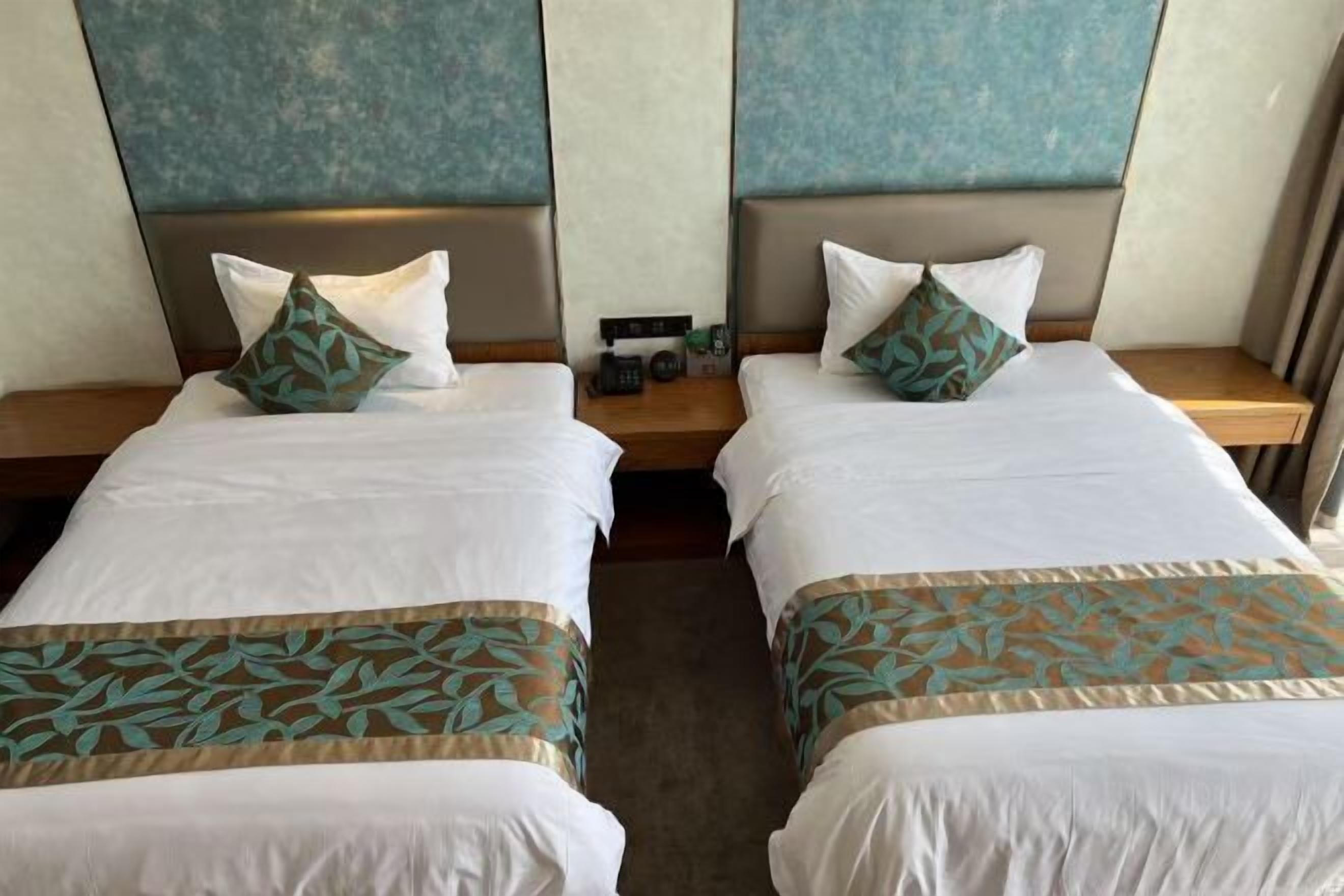 A hotel room with two single beds, each with a pillow and a bedside table.