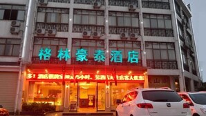 Ein Hotel mit einer großen Schrifttafel in chinesischen Schriftzeichen, mehreren Klimaanlagen und einem weißen Auto vor der Fassade.