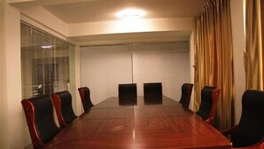 Ein Konferenzraum mit einem großen Holztisch, schwarzen Stühlen, einer weißen Decke und einem Fenster mit Jalousien.