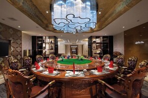 A round table with chairs, a chandelier, and a television screen.