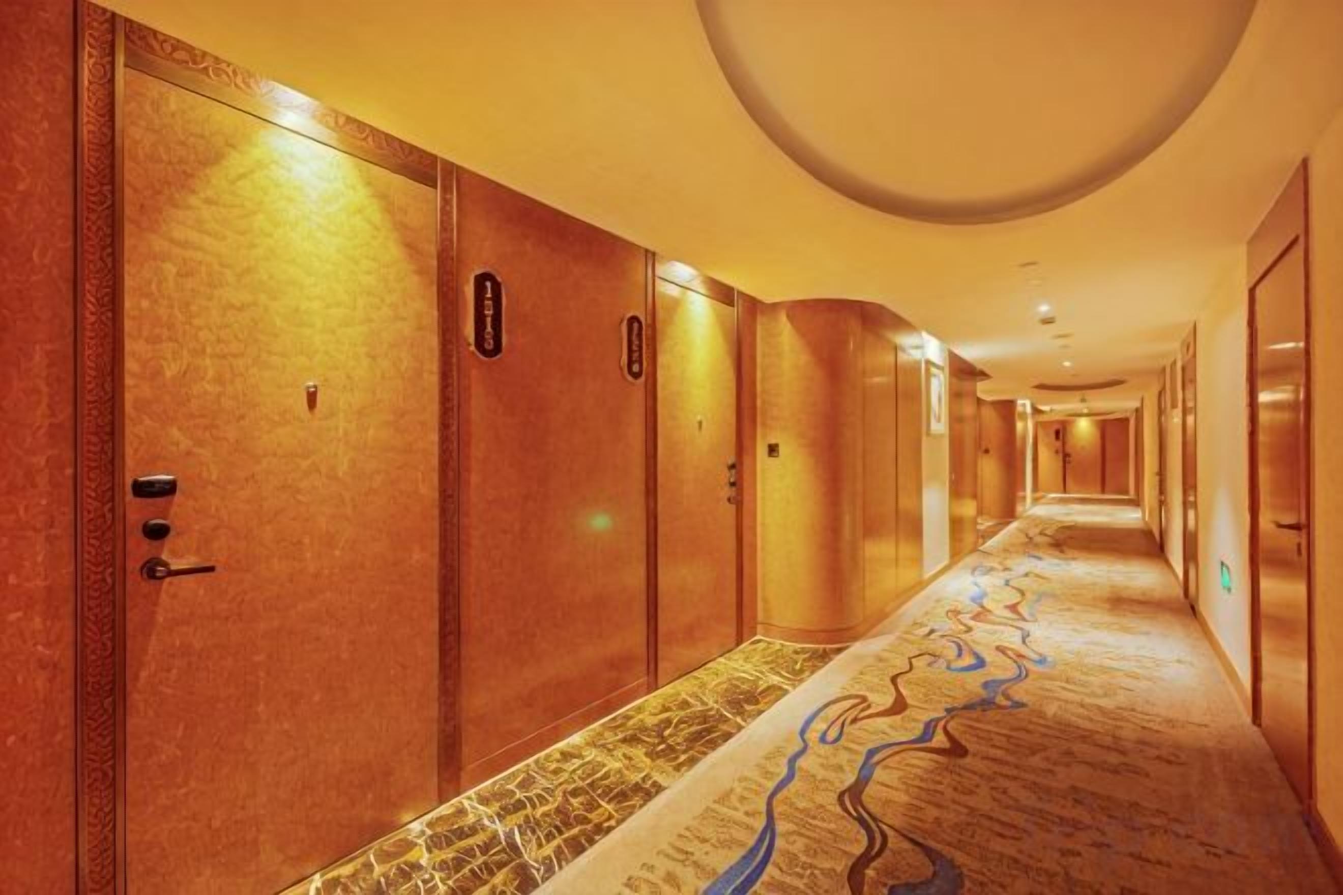 Un couloir d’hôtel avec des portes des deux côtés, une moquette à motifs et un plafond doté d’un éclairage encastré.