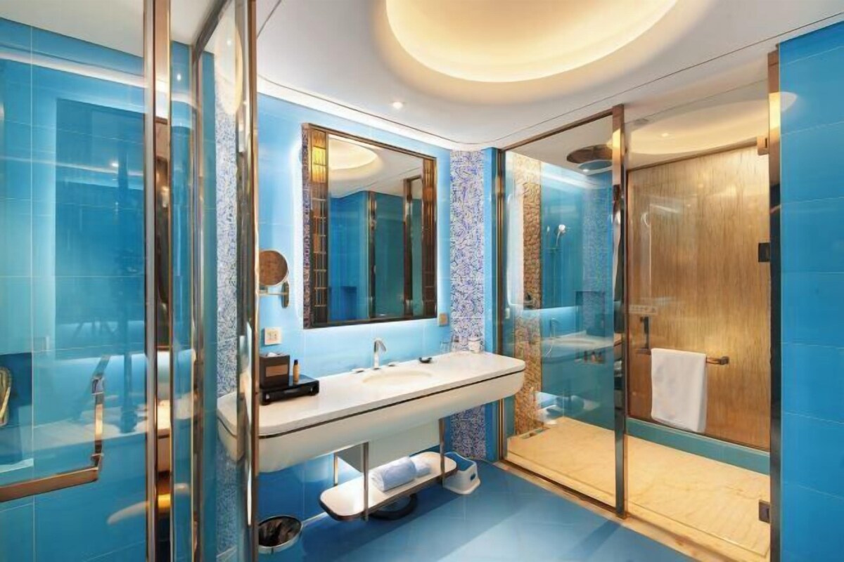 Un baño moderno con ducha envuelta en vidrio, un espejo grande y un lavabo blanco.