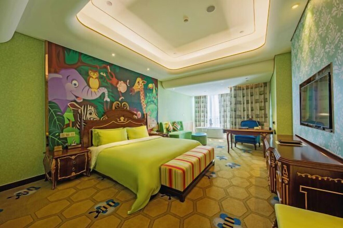 Habitación de hotel con una cama grande, un escritorio, una silla, un televisor y un mural colorido en la pared.