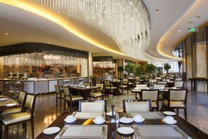 Um restaurante espaçoso com várias mesas para refeições, um bar e um lustre moderno.