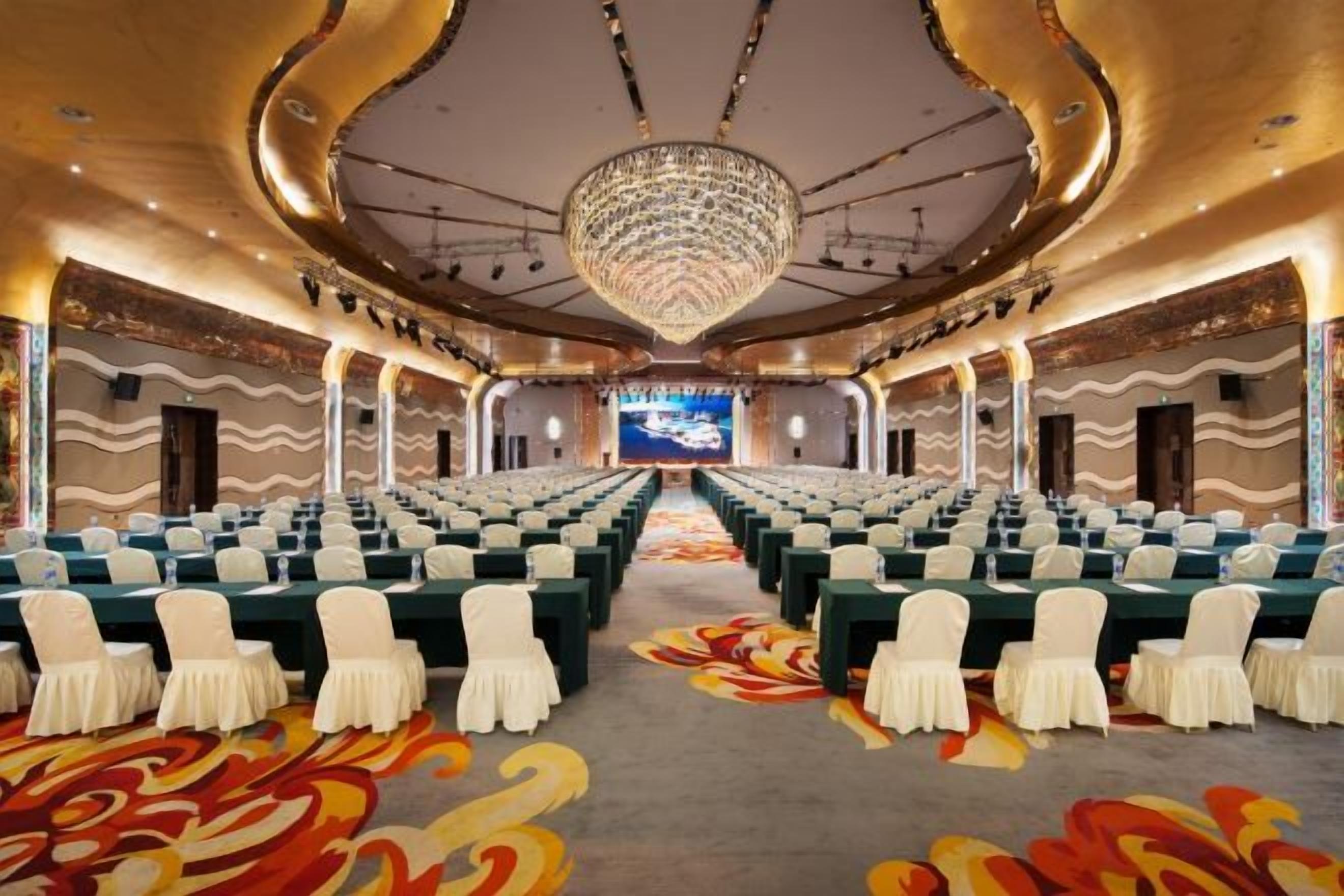 A conference room with rows of chairs, a large screen at the front, and a chandelier.