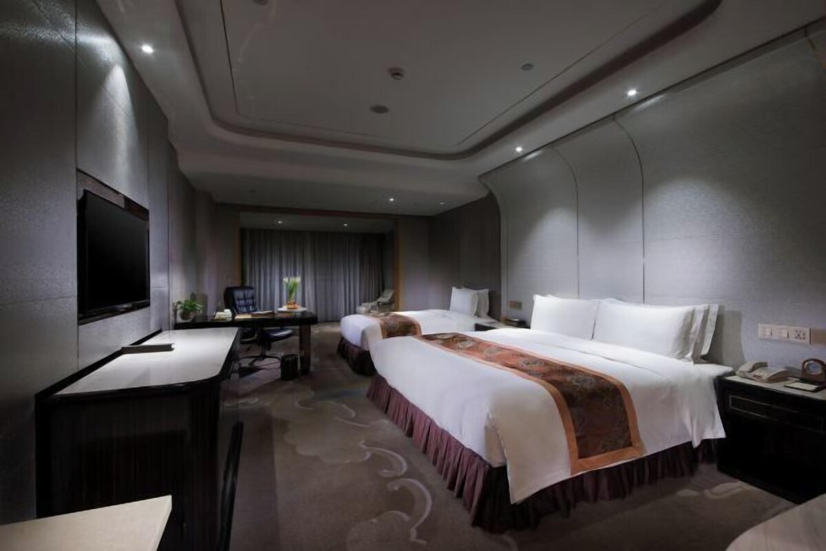 Habitación de hotel con una cama grande, un escritorio, una silla, un televisor y una ventana con cortinas.