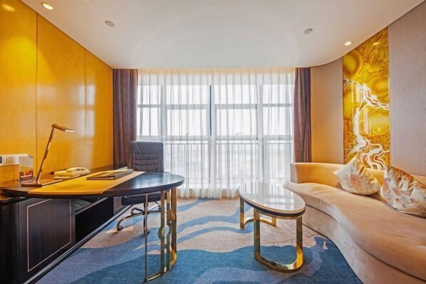 Una habitación de hotel moderna con un escritorio, una mesa redonda, un sofá y un amplio ventanal con cortinas.