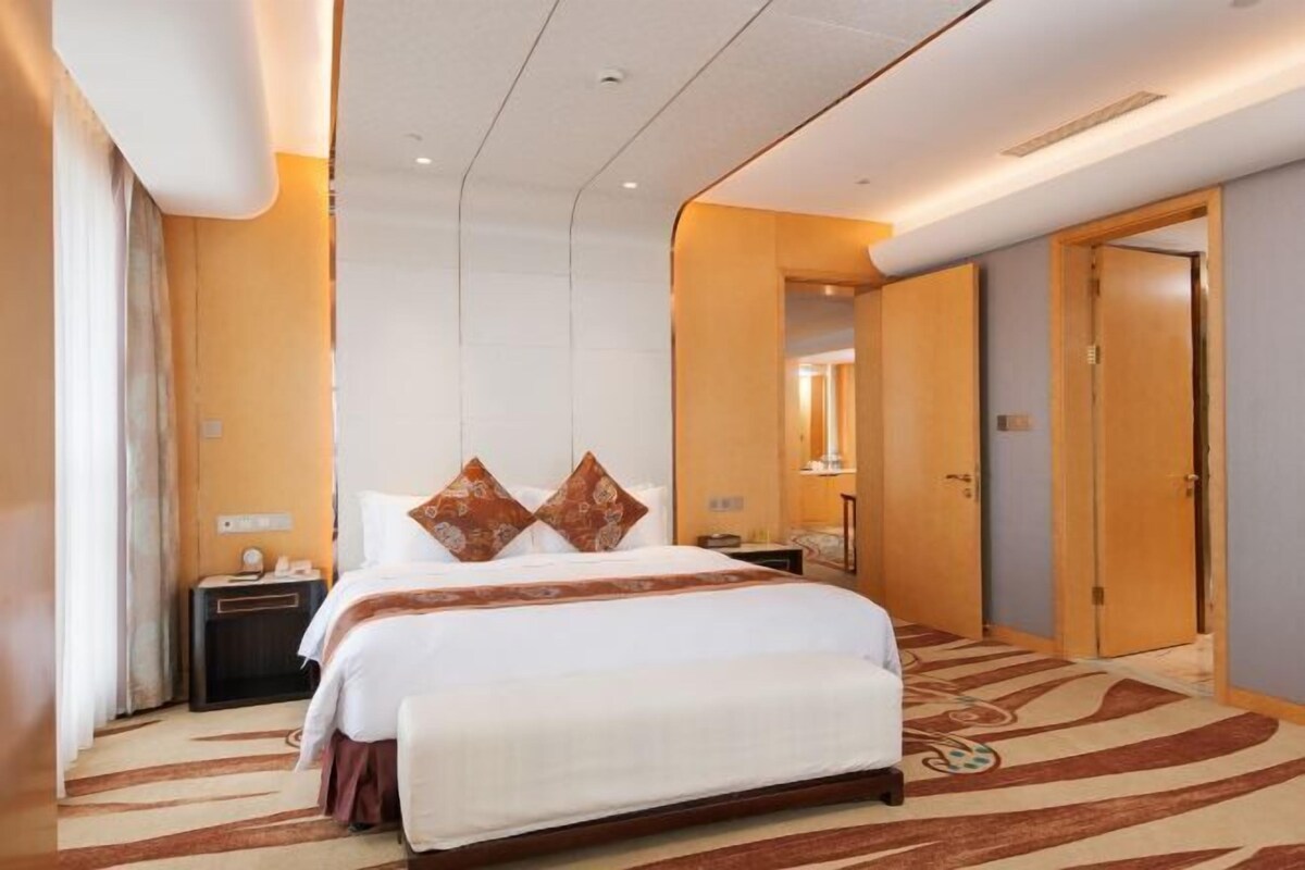 Habitación de hotel con una cama grande, dos mesitas de noche, un tocador, un espejo y una puerta.