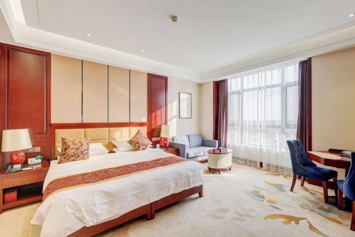 A hotel room with a large bed, a desk, a chair, and a sofa.