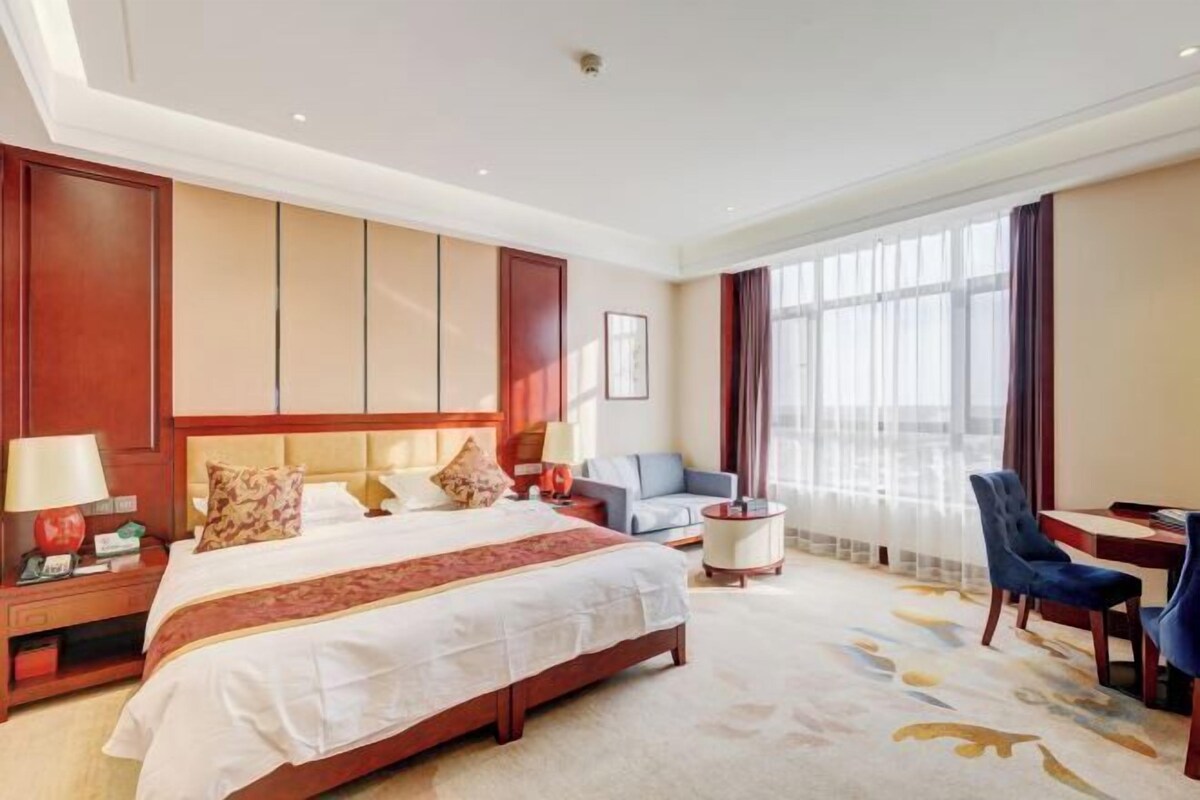 Habitación de hotel con una cama grande, un escritorio, una silla, un sofá y una ventana con cortinas.