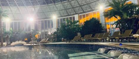 An indoor swimming pool with lounge chairs and a glass ceiling.