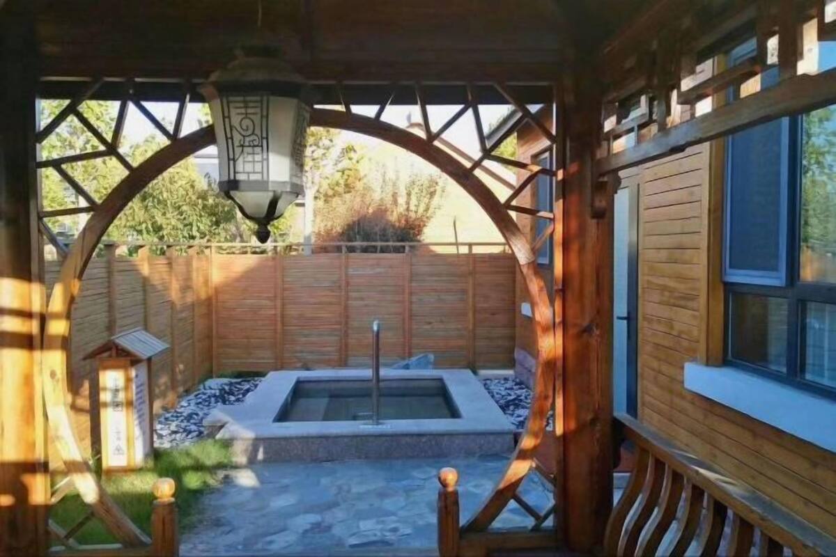 A wooden cabin with a stone patio, a hot tub, and a wooden deck.
