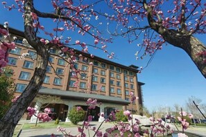 A multi-story hotel with a central courtyard, surrounded by trees with pink blossoms. - Shenghao Seasons Hotel (Huimin)