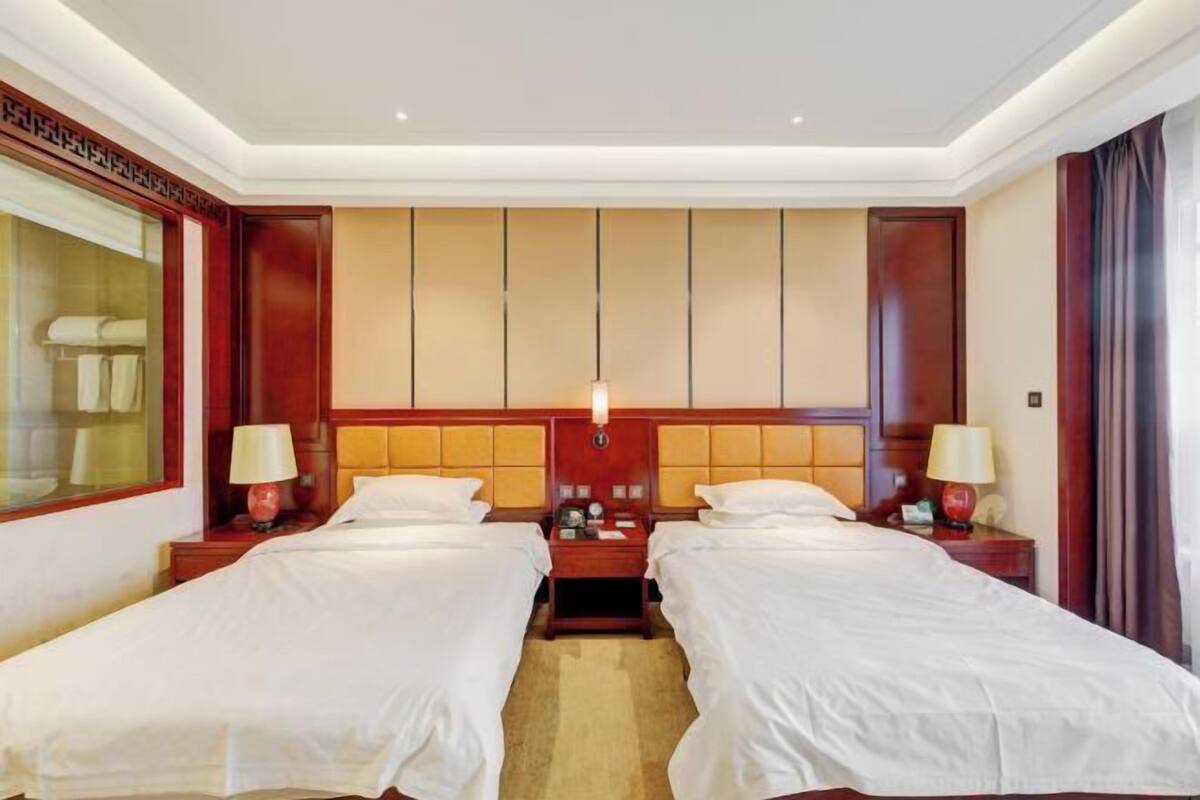 A hotel room with two beds, a large window, and a wooden headboard.