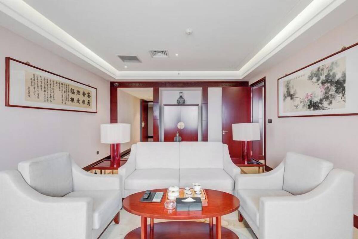 A modern hotel room with a white sofa set, a round wooden coffee table, and two wall-mounted lamps.