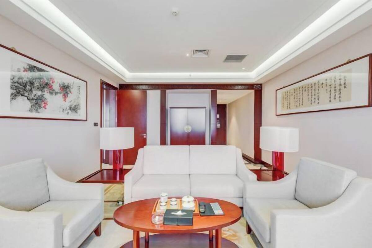 A modern hotel room with a white sofa set, a round coffee table with amenities, and artwork on the walls.