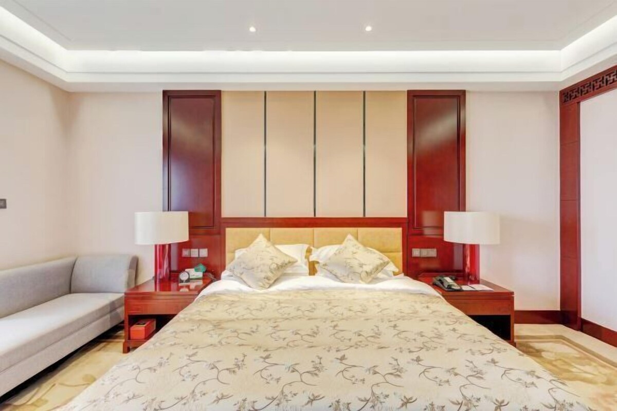 Habitación de hotel con una cama grande, dos mesitas de noche, un sofá y un atril.