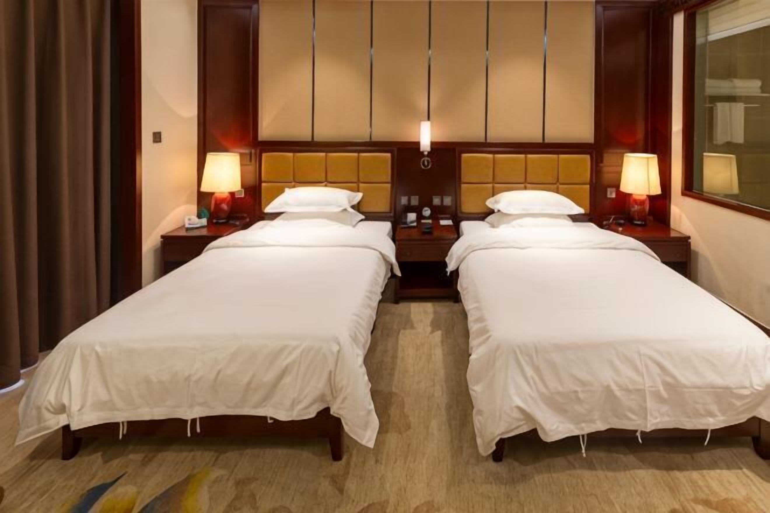 A hotel room with two beds, nightstands, lamps, and a large window.