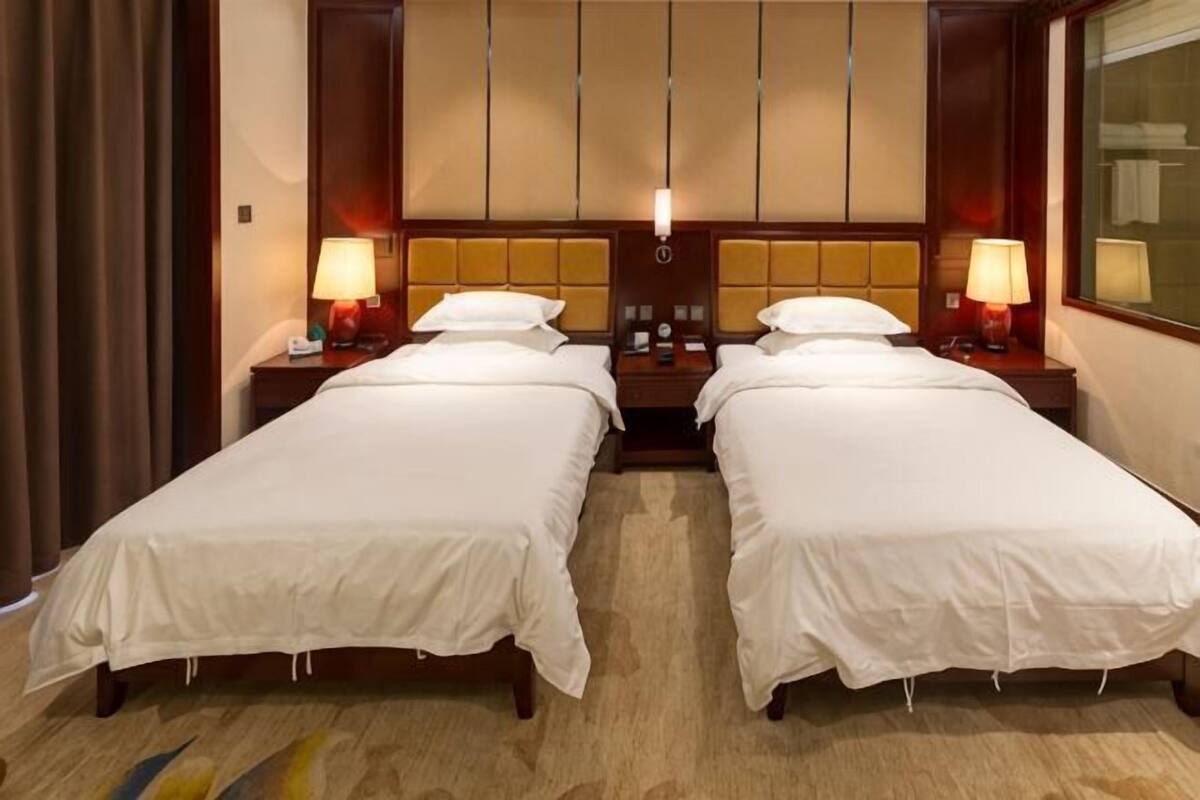 A hotel room with two beds, nightstands, lamps, and a large window.