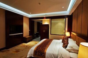 Quarto de hotel com cama, televisão, escrivaninha e janela com persianas.