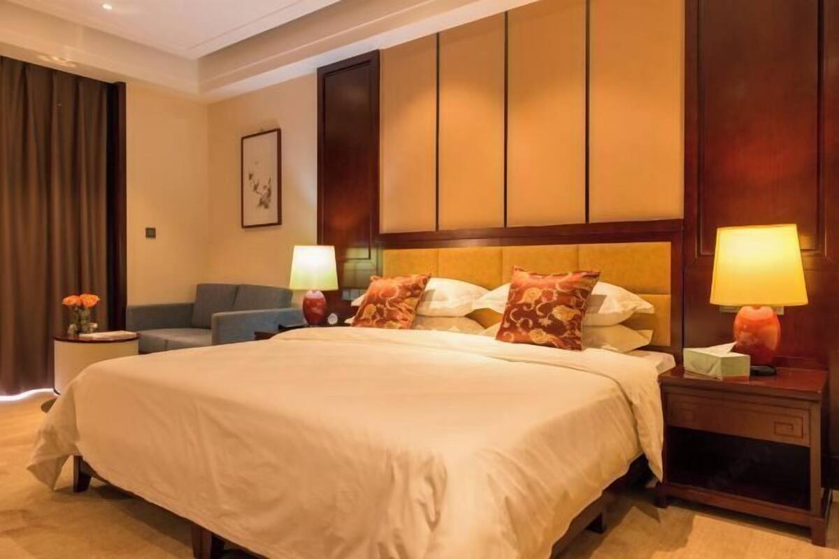 A hotel room with a large bed, two bedside tables with lamps, a sofa, and a wall-mounted artwork.