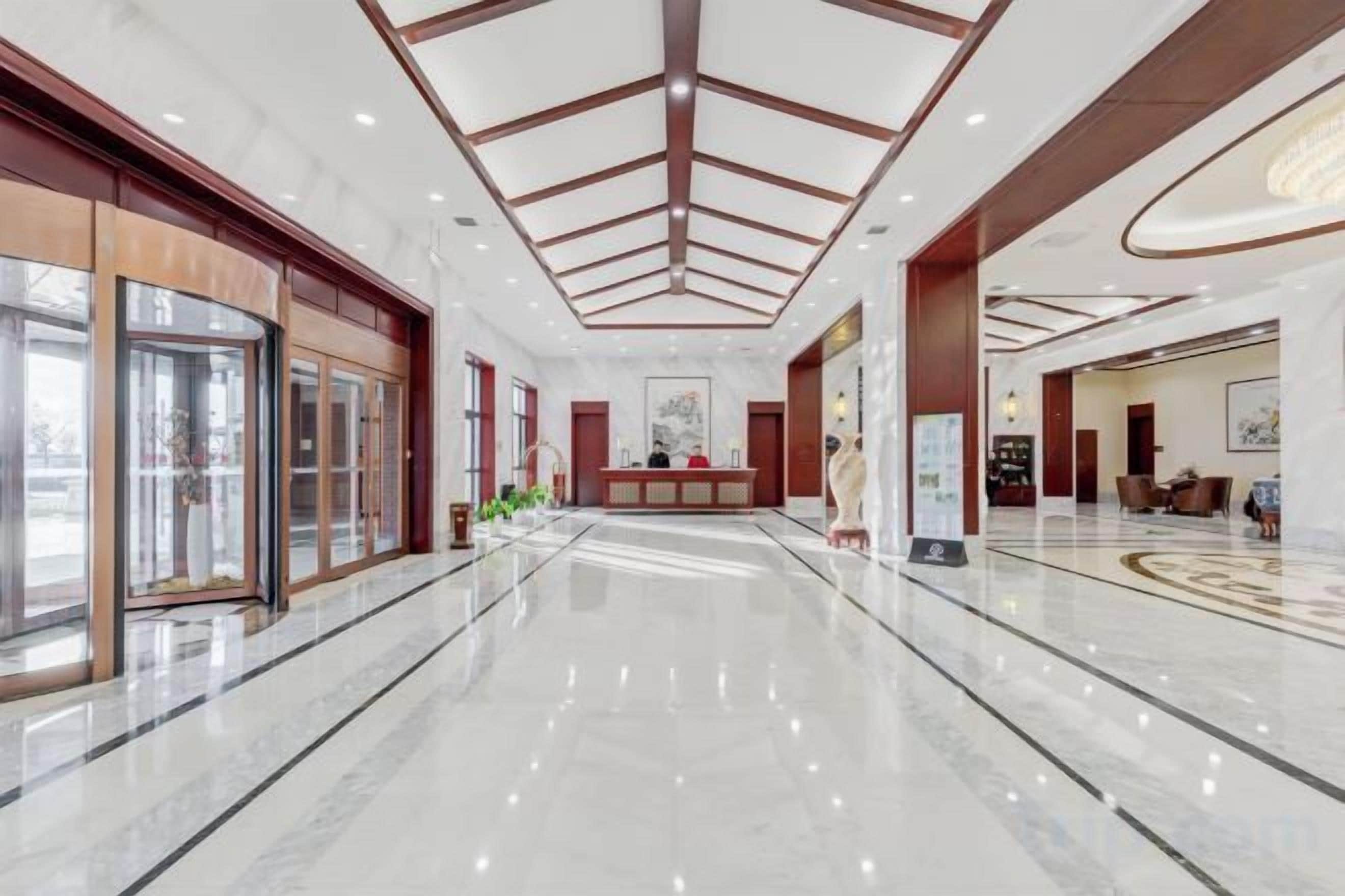 A spacious lobby with a marble floor, a reception desk, and a high ceiling with a geometric design.