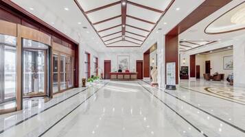A spacious lobby with a marble floor, a reception desk, and a high ceiling with a geometric design.