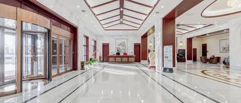 A spacious lobby with a marble floor, a reception desk, and a high ceiling with a geometric design.