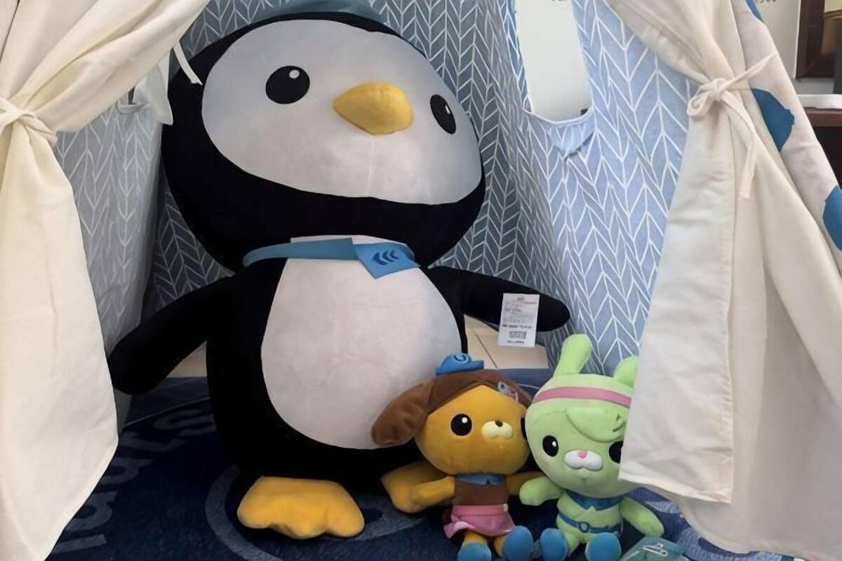 A large plush penguin, a brown bear, and a green alien toy in a tent-like structure.