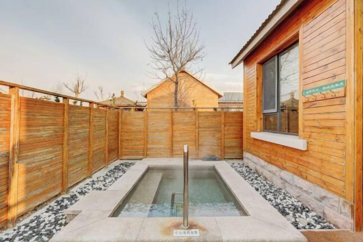 A wooden cabin with a hot tub in the center, surrounded by a wooden fence and a stone pathway.