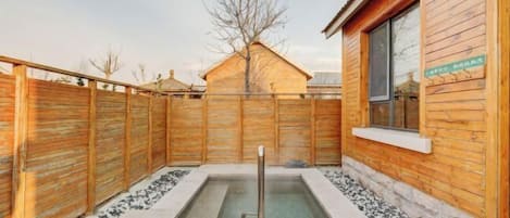 Une cabane en bois avec un jacuzzi au centre, entourée d’une clôture en bois et d’un chemin en pierre.