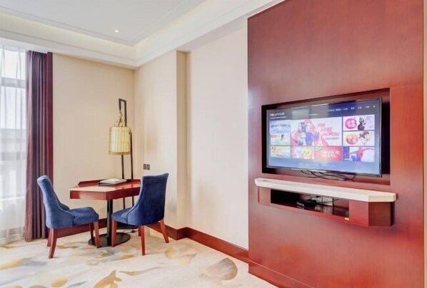 Habitación de hotel con una televisión de pantalla plana montada en una pared de madera, un escritorio con dos sillas y una lámpara.