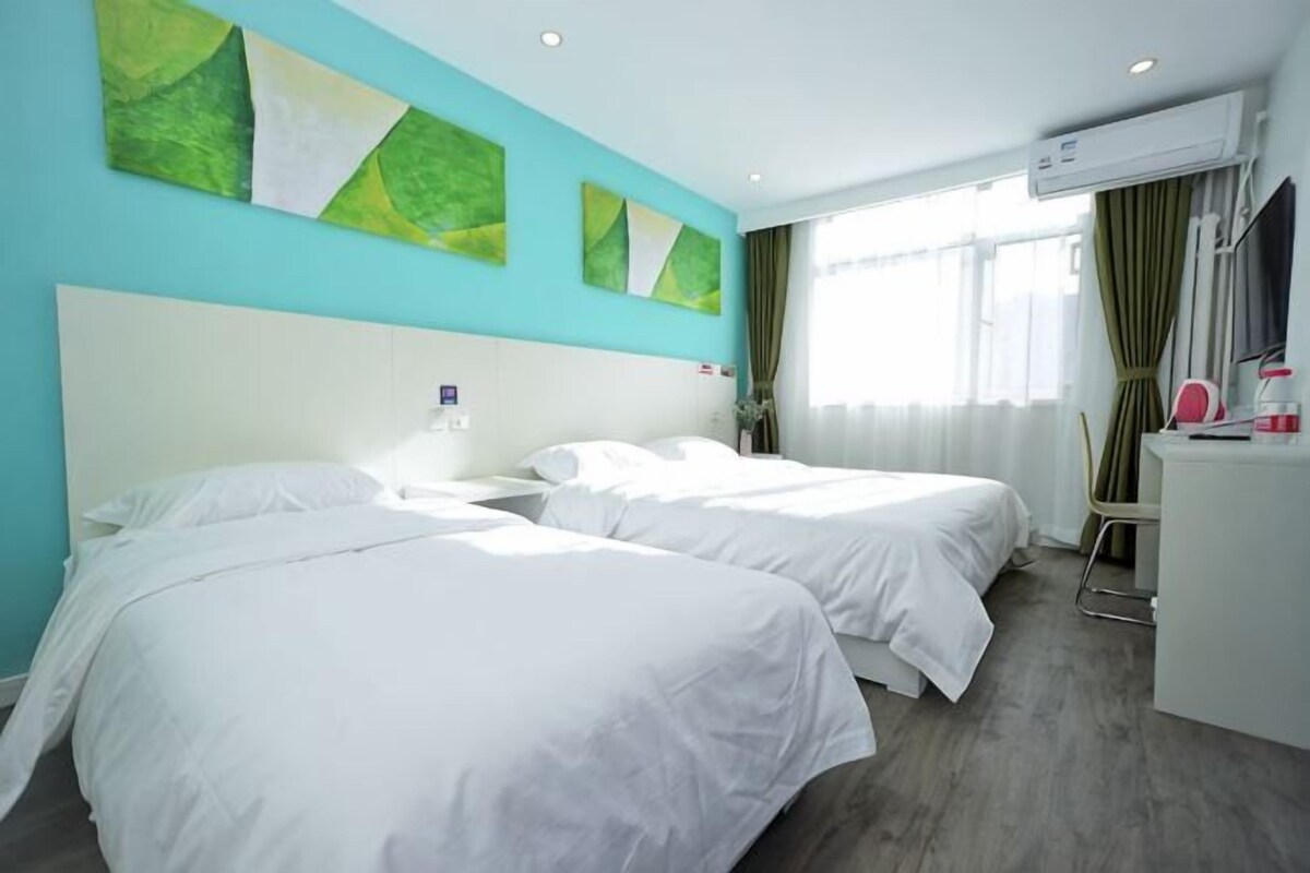 A hotel room with two beds, a desk, and a window with curtains.