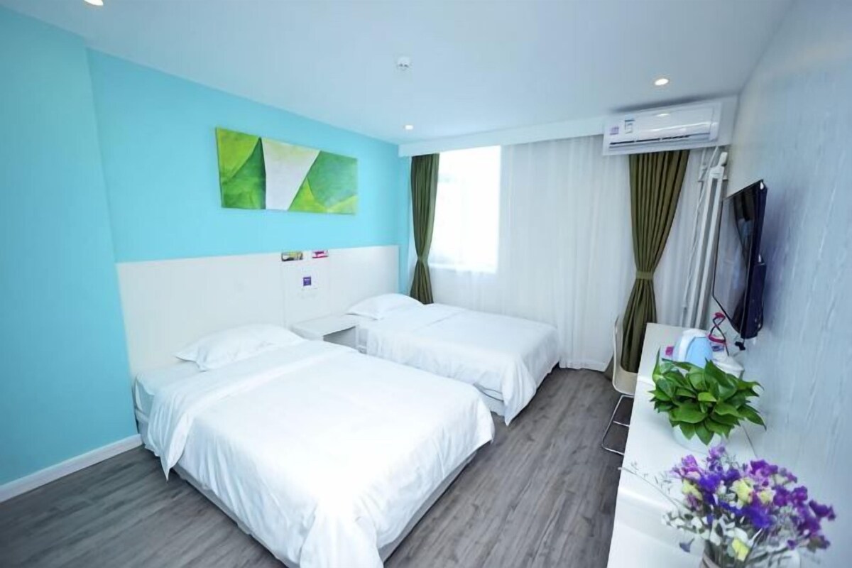 A hotel room with two beds, a flat-screen TV, an air conditioning unit, and a window with curtains.