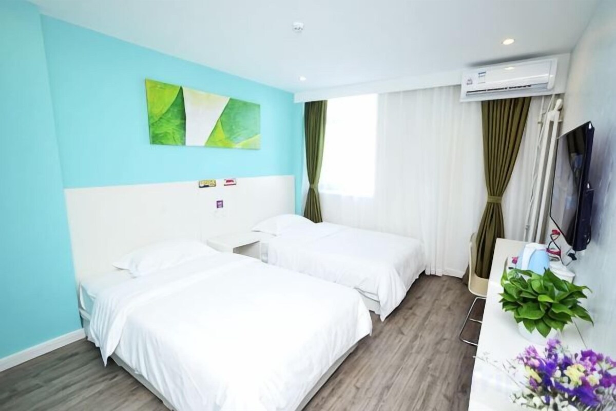 A hotel room with two beds, a desk with a plant, a TV, and a window with curtains.