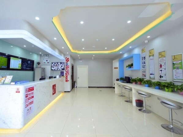 A modern reception area with a white reception desk, a digital screen, and a wall with informational posters.