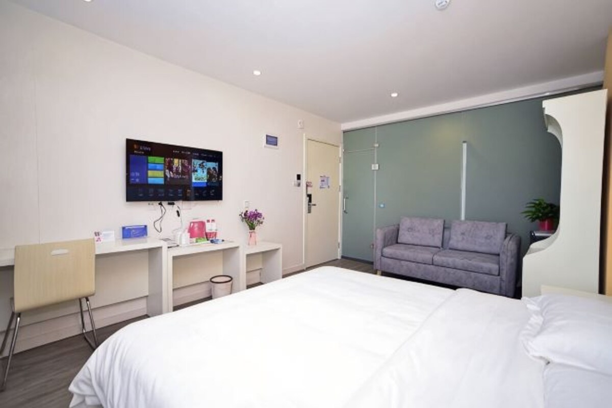 A hotel room with a bed, a desk with a computer, a television, and a couch.