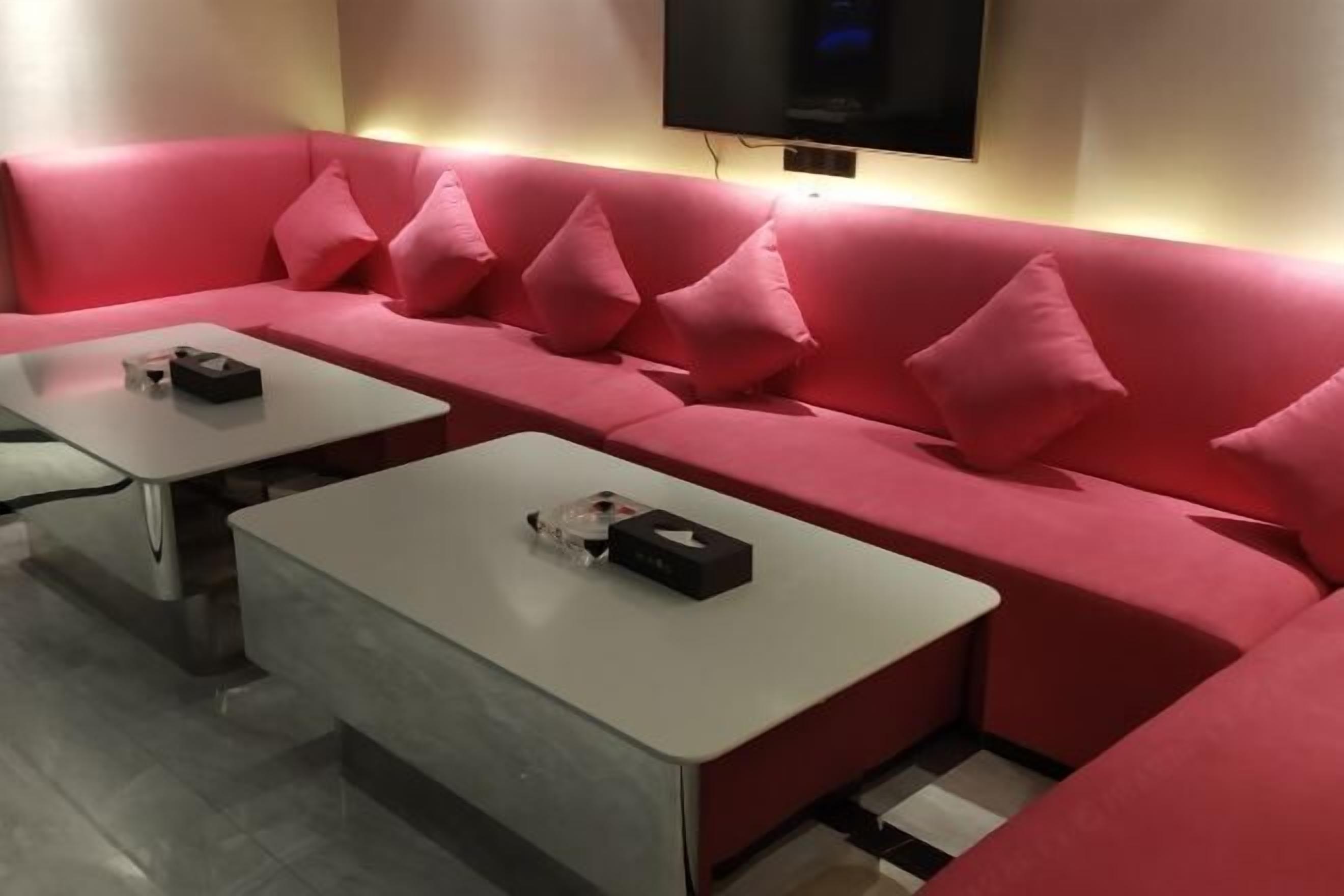 A modern living room with a red sofa, two white coffee tables, and a flat-screen TV mounted on the wall.