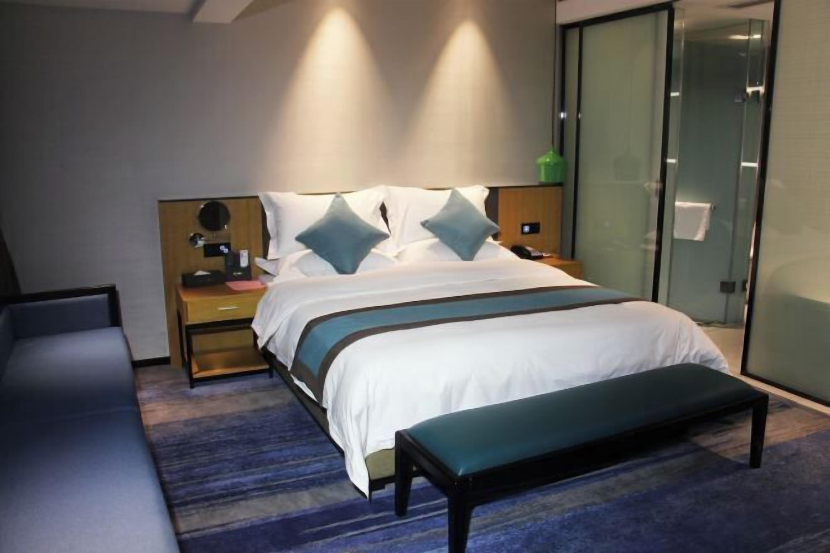 Una habitación de hotel moderna con una cama, mesitas de noche, un banco y un separador de vidrio.