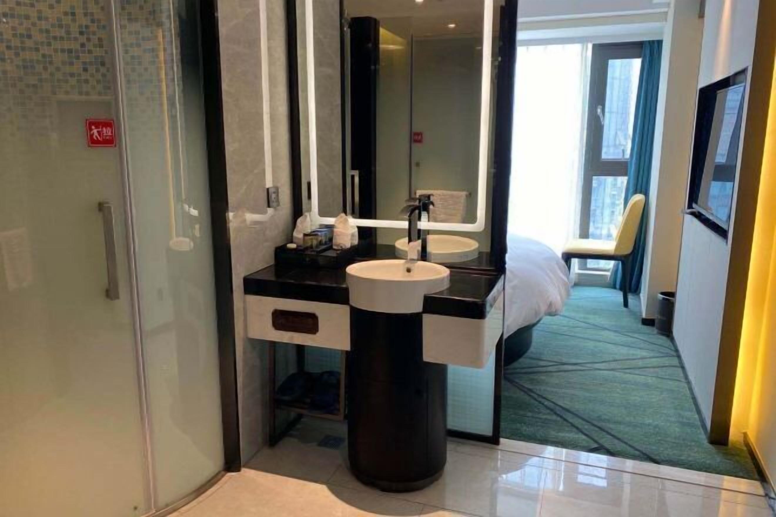 Une salle de bain d’hôtel moderne, dotée d’une douche à parois de verre, d’un lavabo rond et d’un grand miroir.