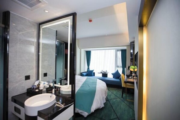 A hotel room with a large mirror, a bed with a green and white bedspread, a desk with a lamp, and a window with curtains.