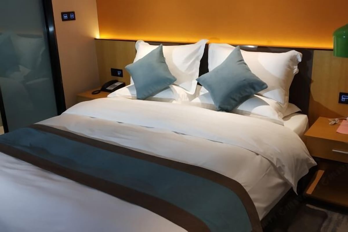 A hotel room with a neatly made bed, a bedside telephone, and a small table with a lamp.