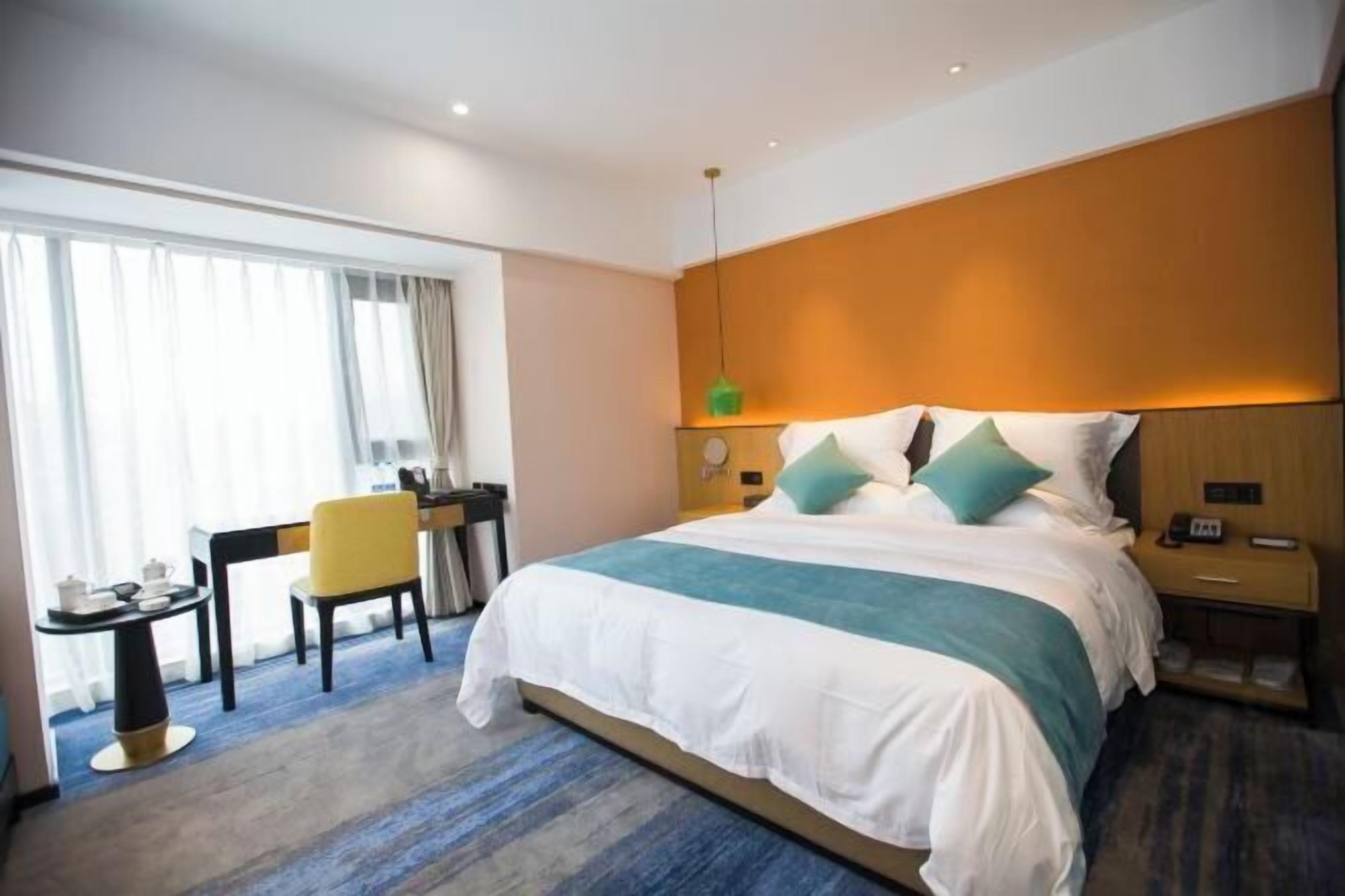 A hotel room with a large bed, a desk with a chair, a small table with a lamp, and a nightstand with a phone.