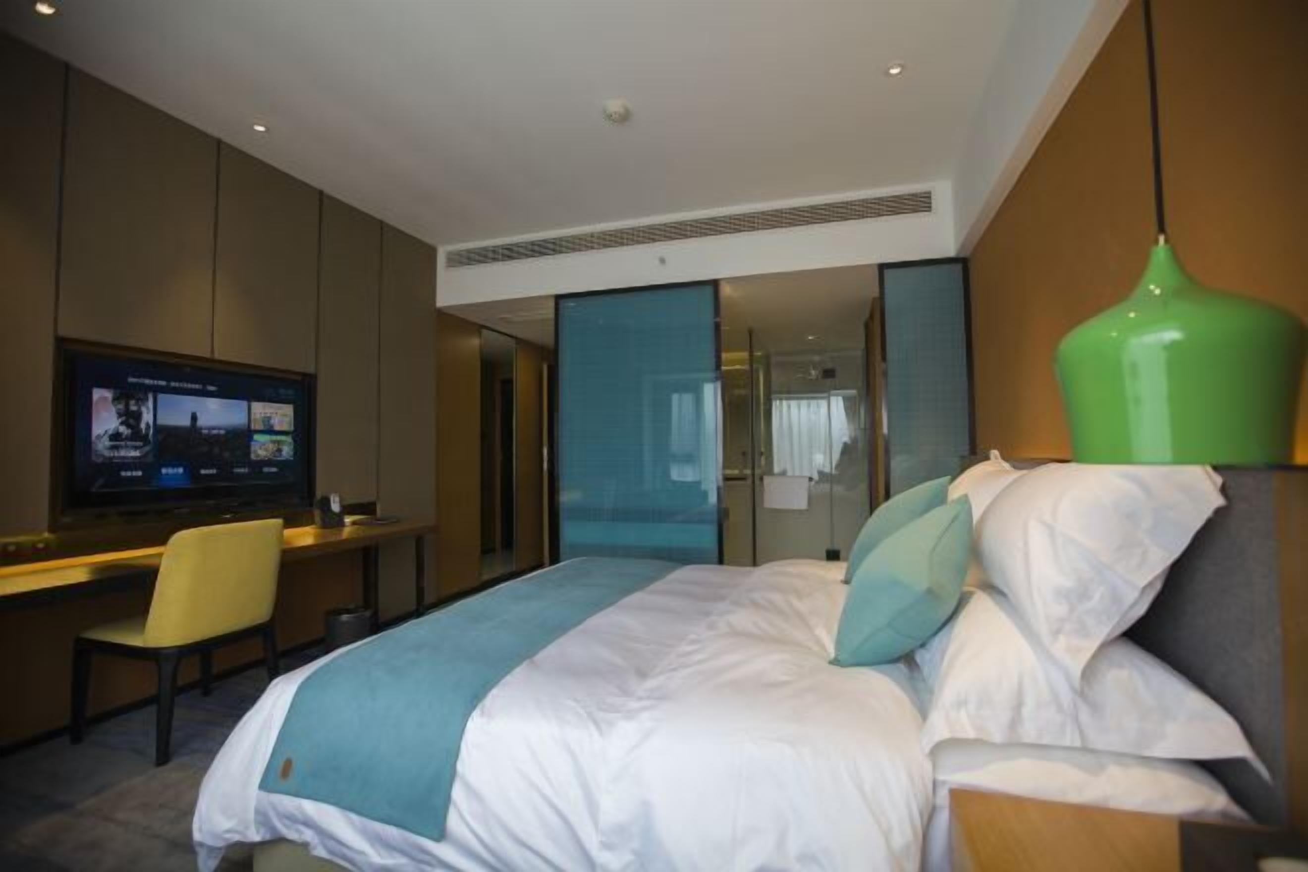 Une chambre d’hôtel avec un lit, un bureau, une télévision et une lampe suspendue verte.