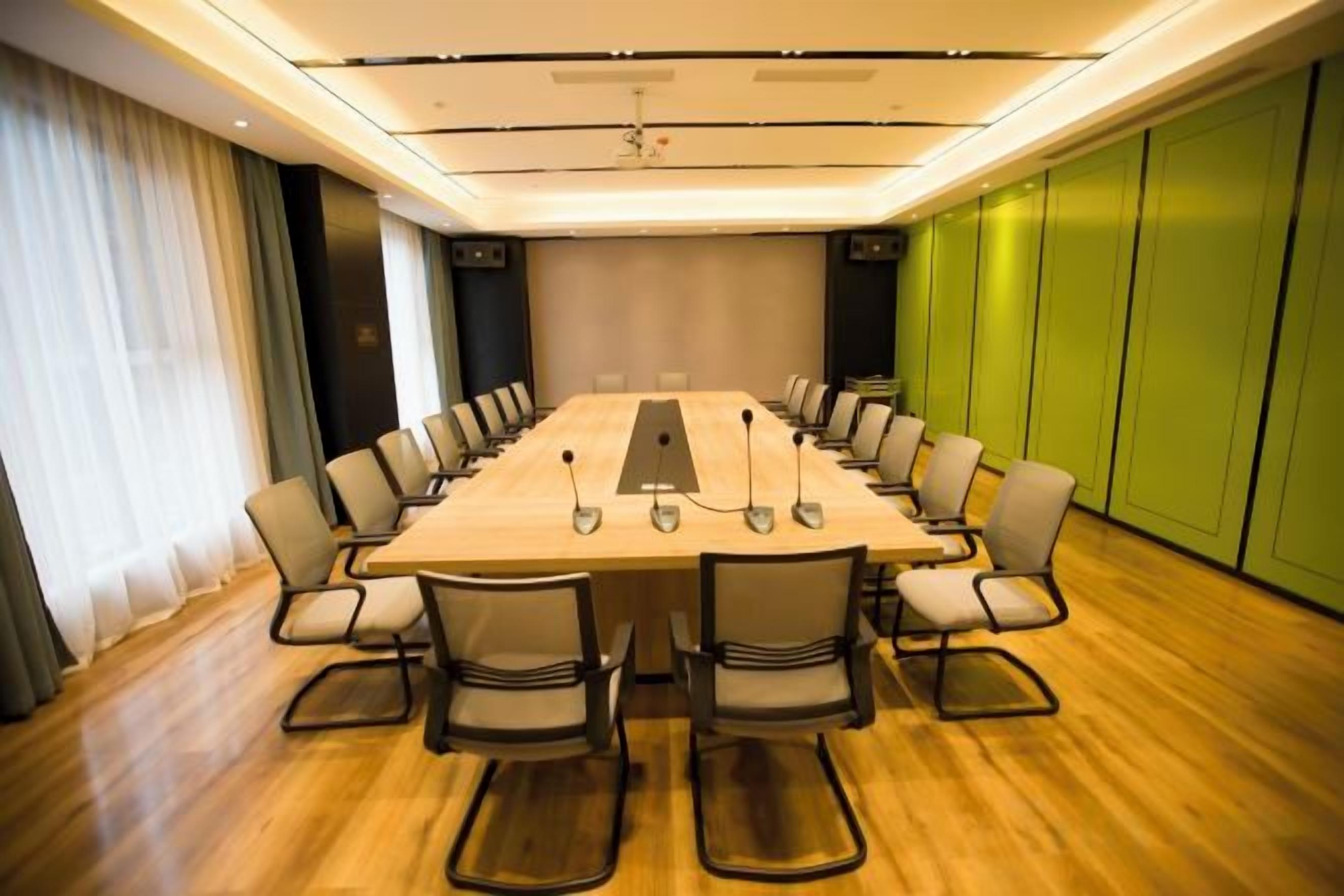 Un salón de conferencias con una larga mesa, sillas, micrófonos y una pantalla de proyector.