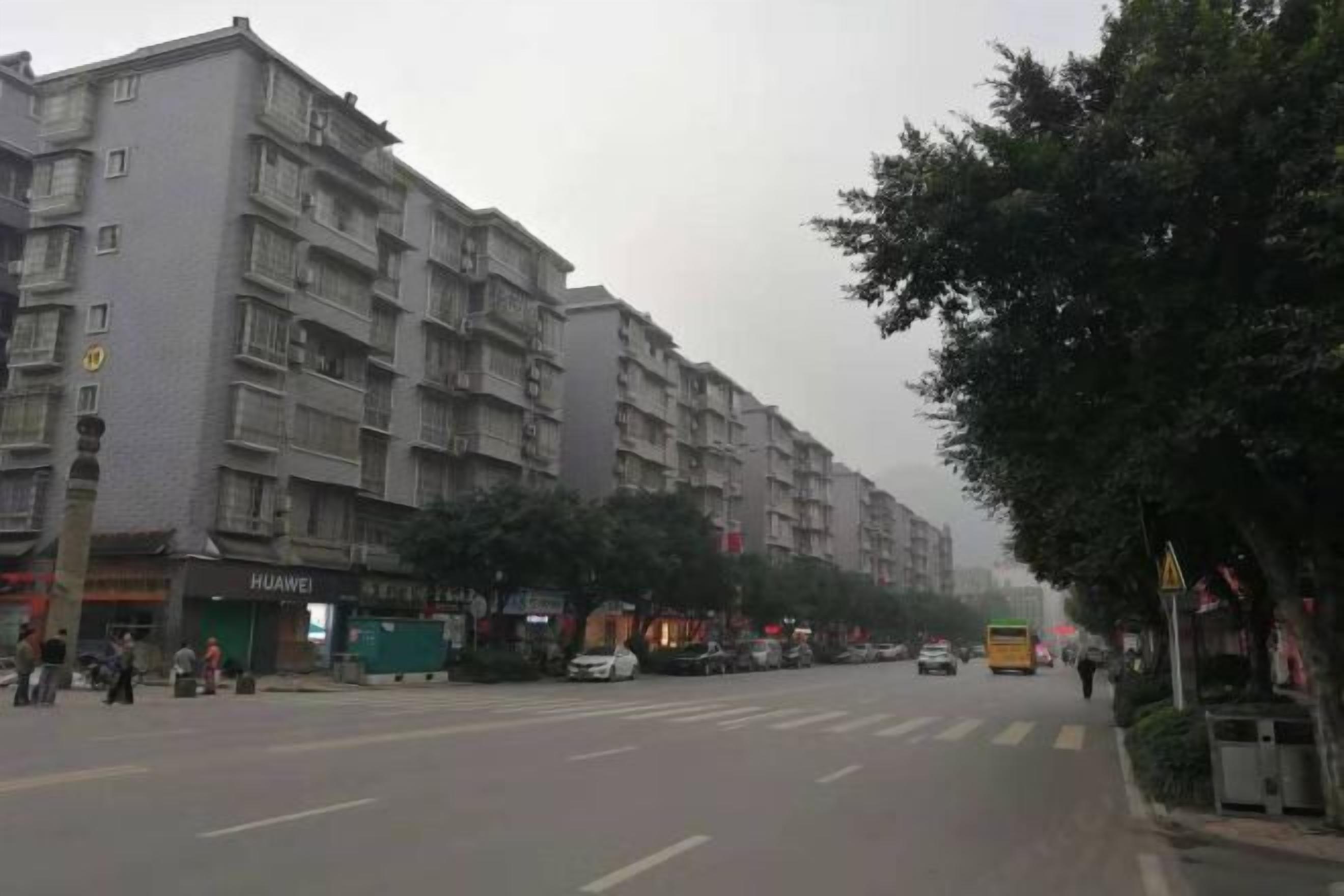 A multi-story residential building with balconies, a Huawei store, and a street with parked cars and a bus.