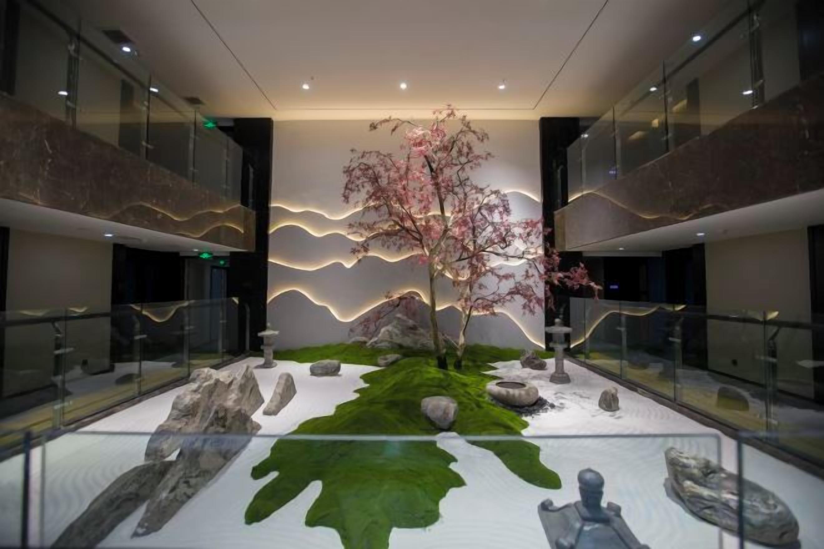 A modern interior with a central garden area featuring a tree, rocks, and a water feature.