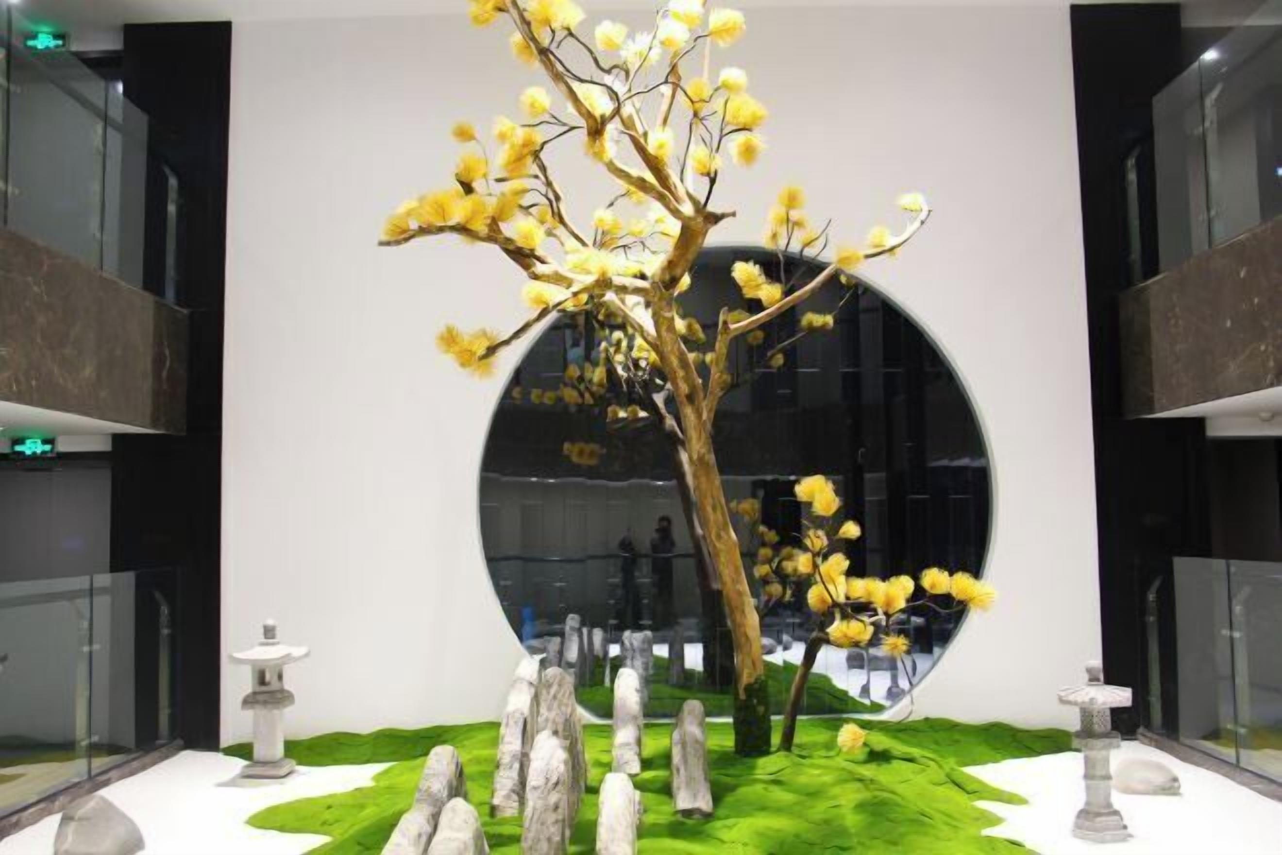 A modern indoor garden with a central tree, stone sculptures, and a circular reflective wall.