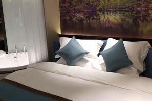 A hotel room with a bed, a painting of a lake, and a bathroom with a sink and mirror. - Yunman Life Hotel (Xuyong)