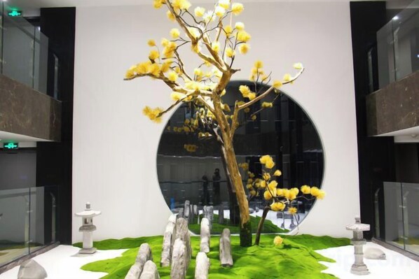 A modern interior with a circular reflective wall, a minimalist tree sculpture, and a stone lantern.
